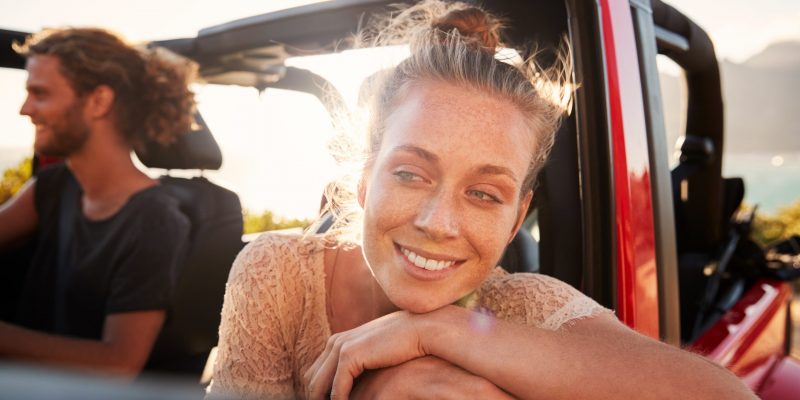 Millennial white couple on a road trip driving in open top car, women leaning on car door, close up Millennial white couple on a road trip driving in open top car, women leaning on car door, close up