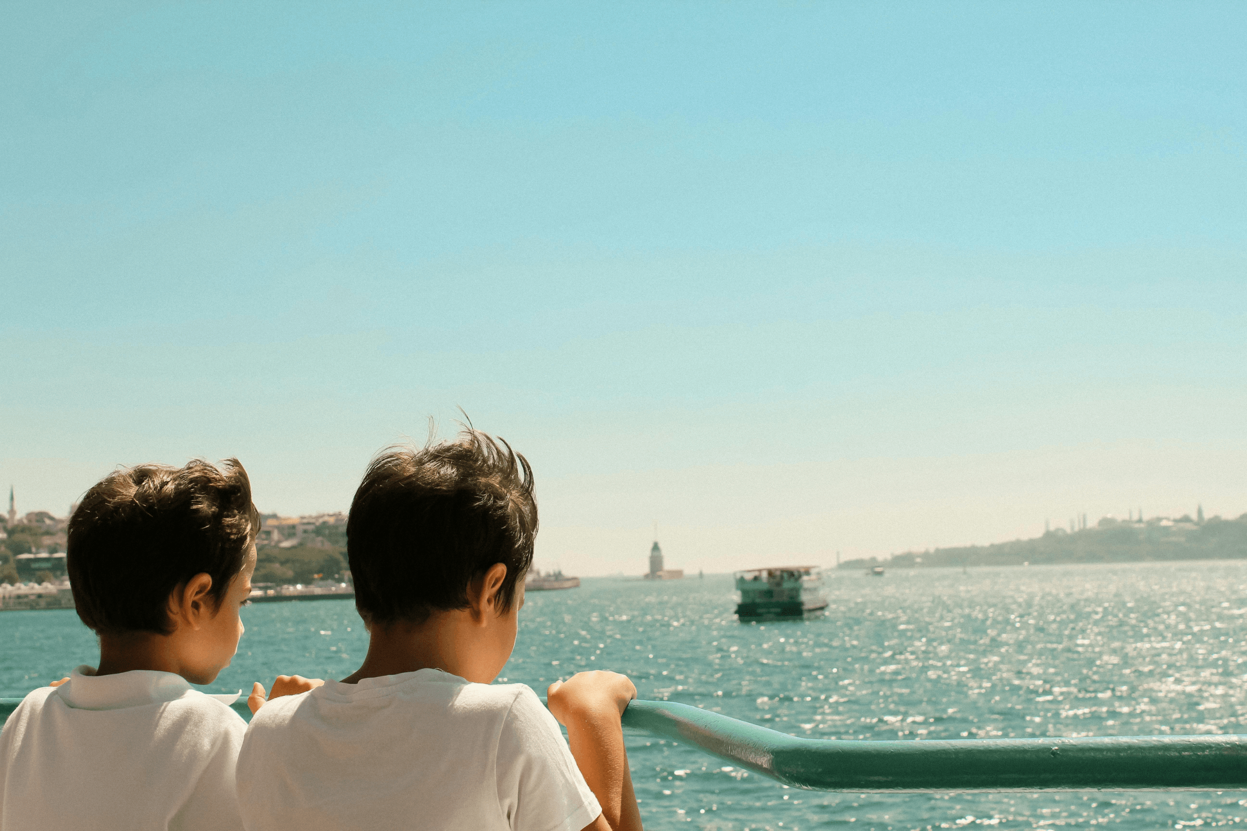 Zwei Kinder stehen auf einer Fähre und schauen übers Meer